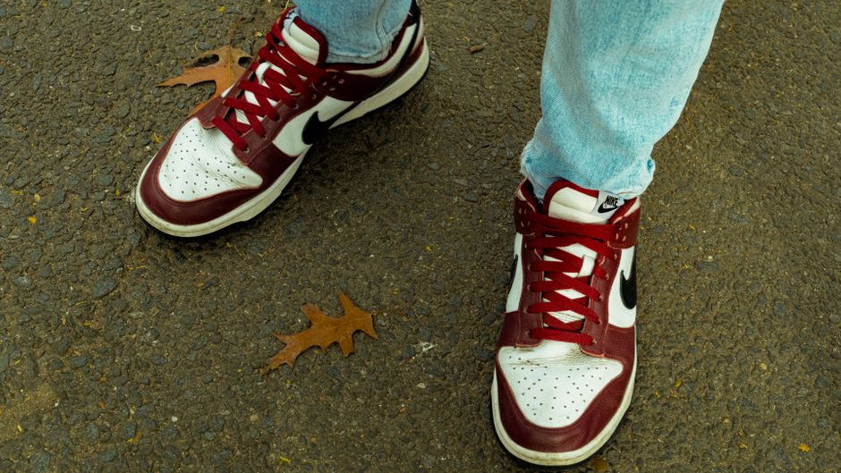 A close-up of red and white sneakers on a textured pavement with autumn leaves.