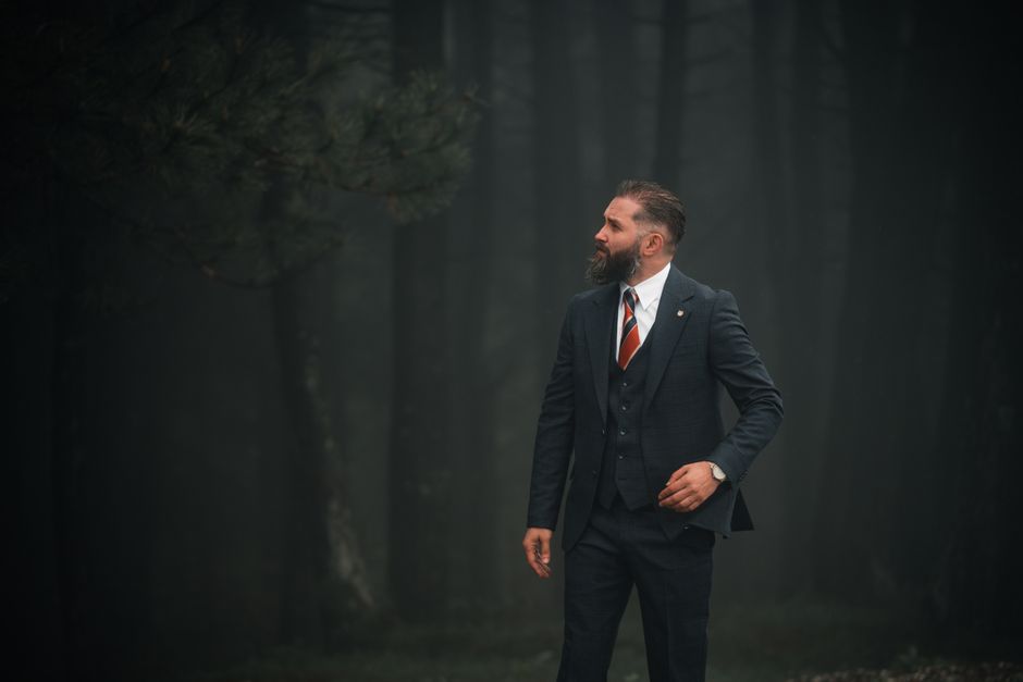 A man in a suit stands confidently in a misty forest, exuding elegance.