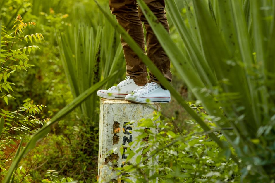 A person stands on a concrete block wearing white sneakers and brown pants surrounded by l