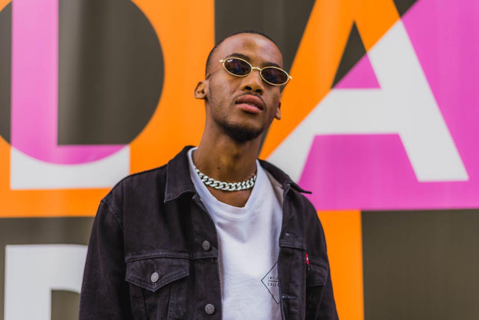 Stylish man in sunglasses and chain necklace against colorful urban background.