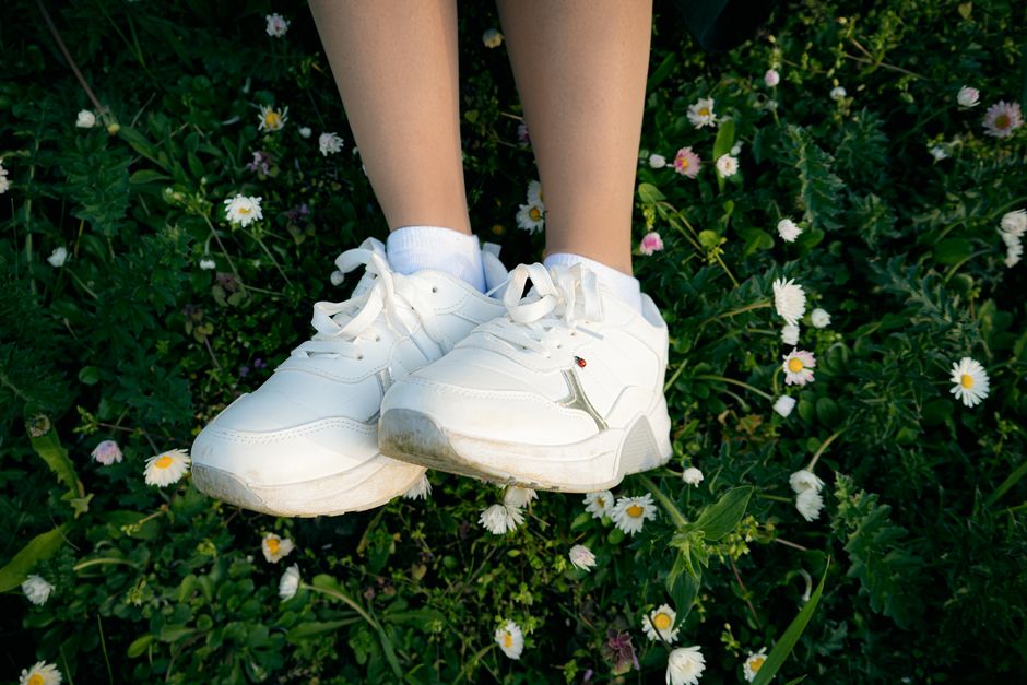 Close-up of white sneakers on grass surrounded by daisies, symbolizing nature and casual lifestyle.