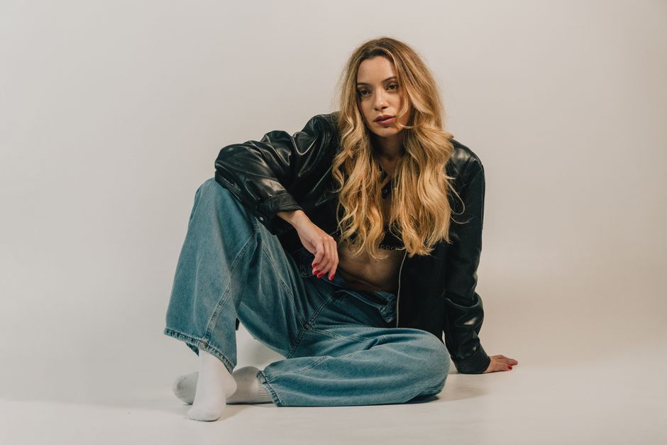 Fashion-forward woman sitting casually in denim and leather jacket.