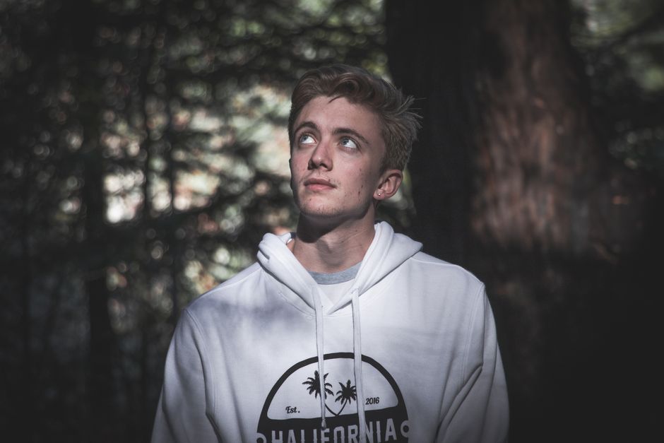 Pensive young man with blond hair looking up in a forest setting.