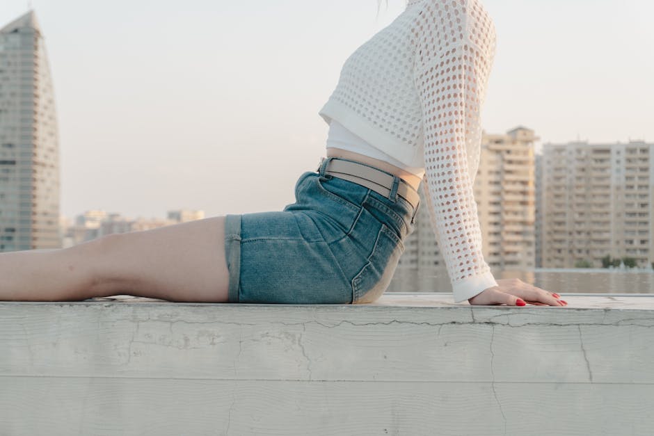 Young woman in stylish denim and white top relaxing on city rooftop at sunset.