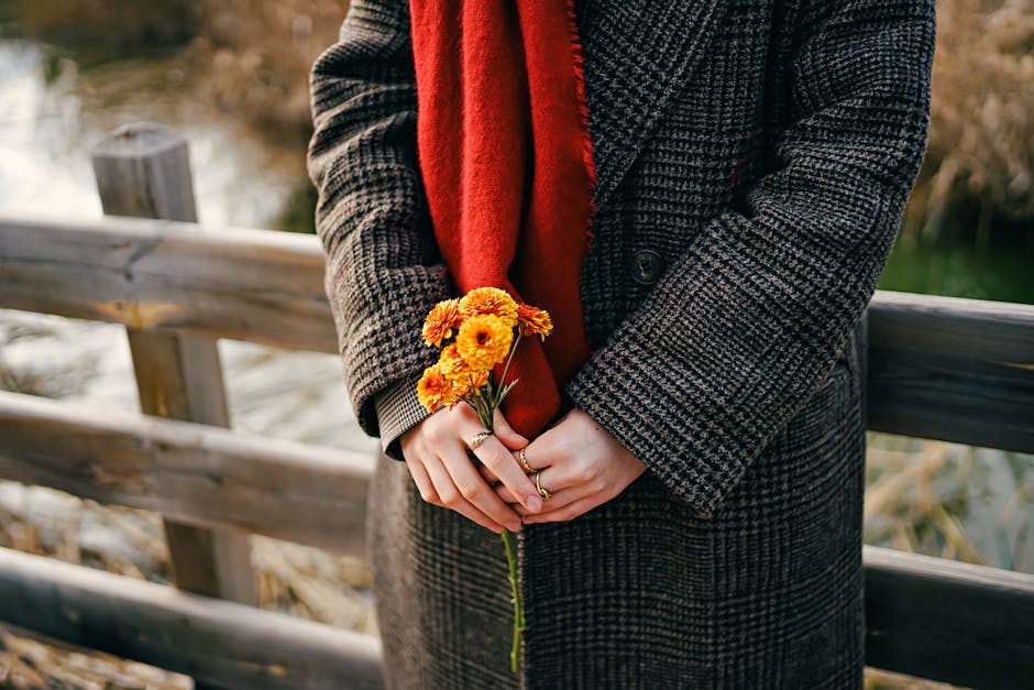 Close-up of woman in coat holding marigold flowers with rustic background, autumn vibes.