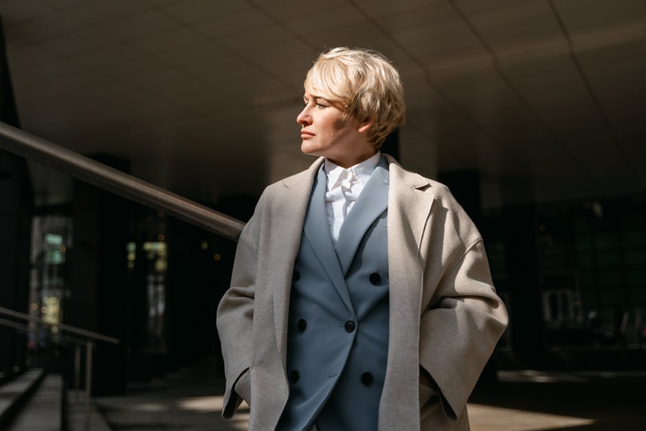 Stylish businesswoman with short hair in a coat, standing confidently outdoors in urban environment.