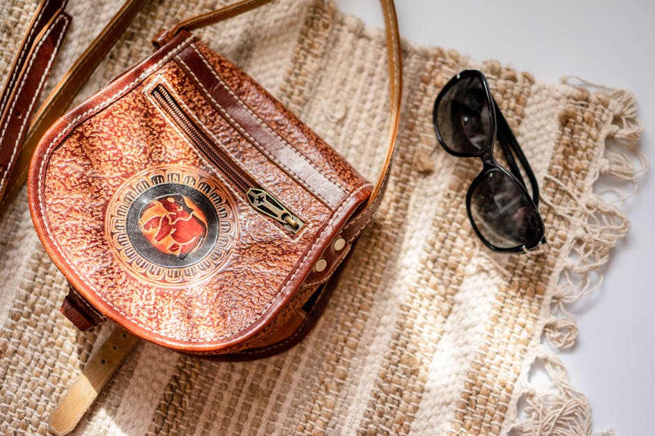 Close-up of a leather handbag and sunglasses on a woven rug with textured pattern.