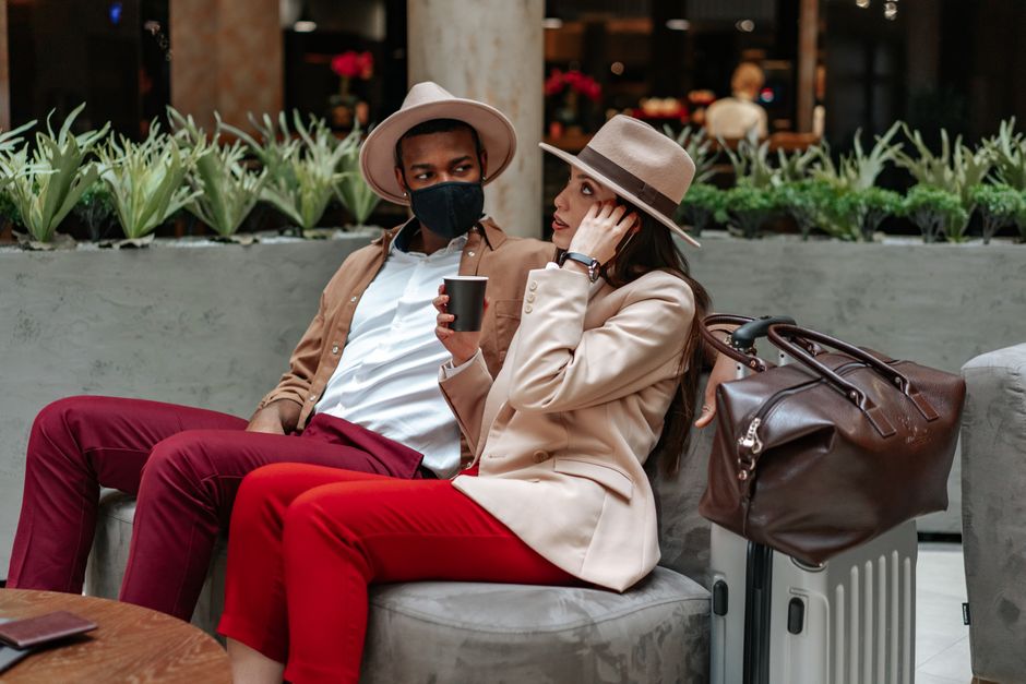 Fashionable couple seated with luggage, enjoying coffee in a chic indoor café setting.