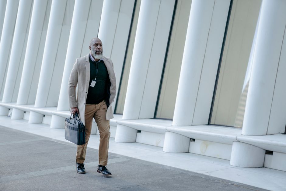 A mature man in business attire walking by contemporary white pillars in a cityscape.