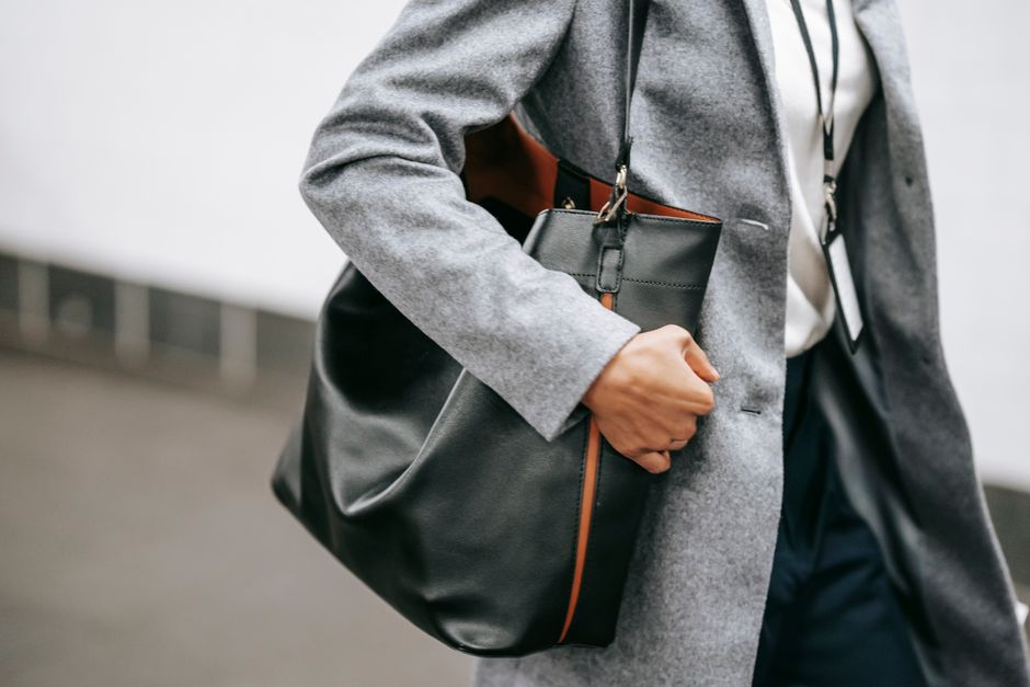 Crop faceless female entrepreneur in stylish classy outfit with bag and name tag walking on city street