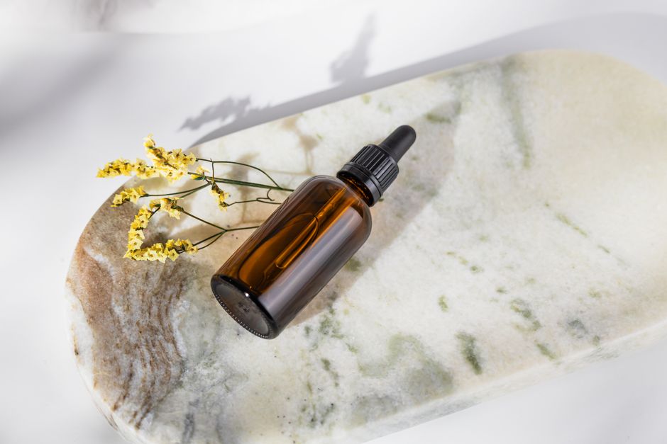 Elegant close-up of a brown dropper bottle with yellow flowers on a marble plate, ideal for cosmetic ads.