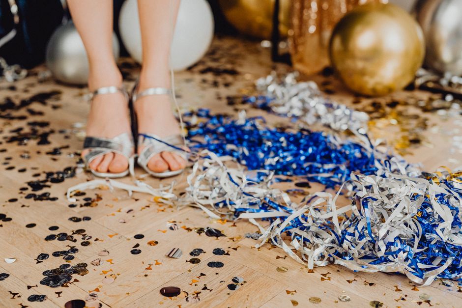 Festive party scene with confetti, balloons, and silver sandals on a wooden floor.