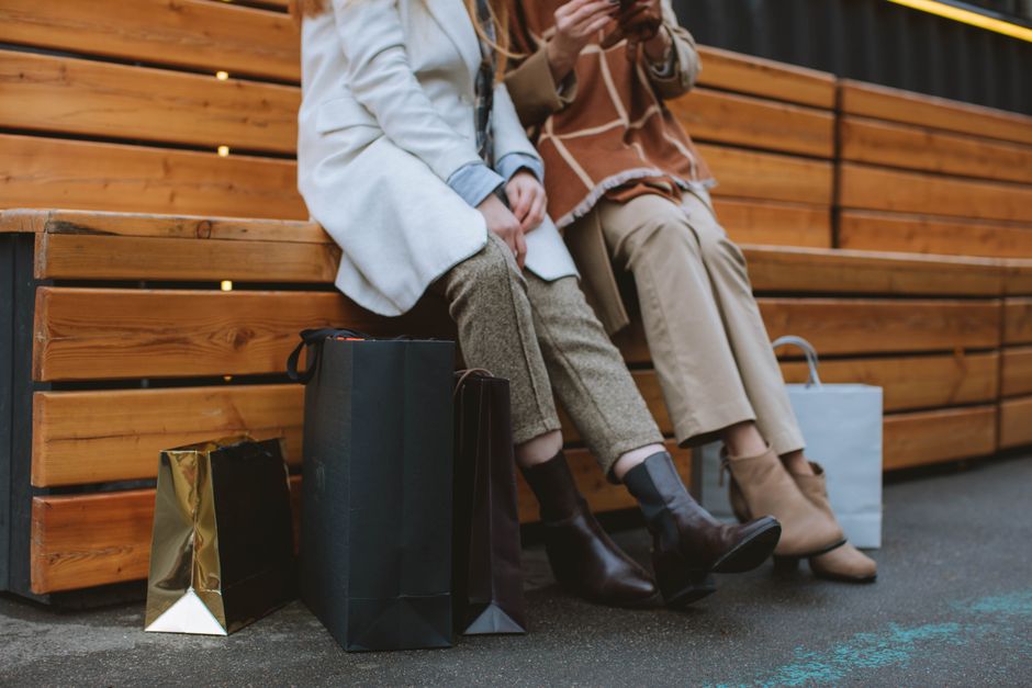 Two fashionable women seated on a bench surrounded by shopping bags, showcasing a stylish urban lifestyle.