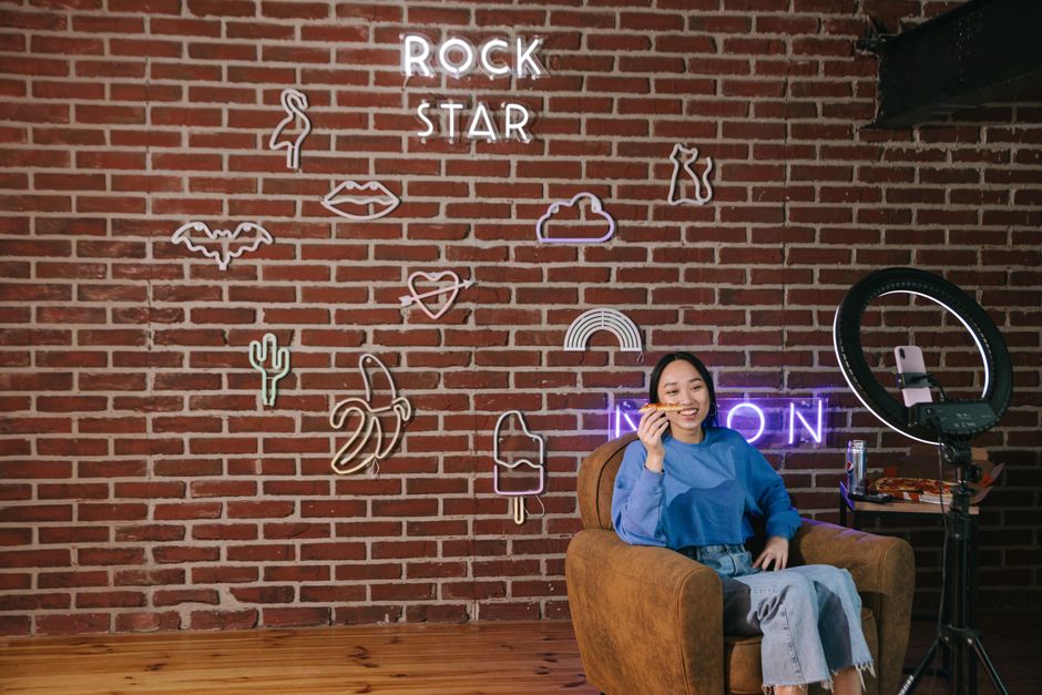 Asian woman streaming content with neon signs on a brick wall. Modern influencer setup.