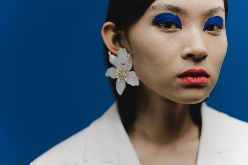 Portrait of a woman with bold blue eyeshadow and red lips against a blue background.