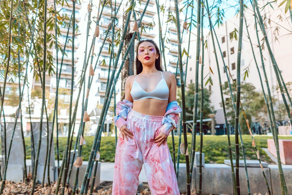Stylish young woman posing confidently among bamboo trees in an urban outdoor setting.