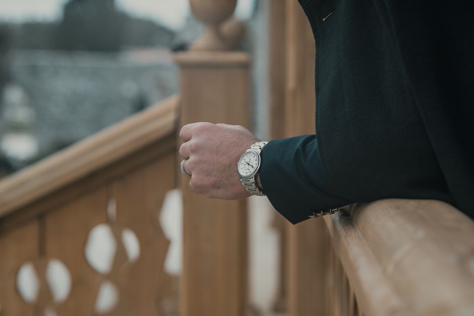 Elegant close-up of a man's hand wearing a wristwatch, leaning on a wooden railing.