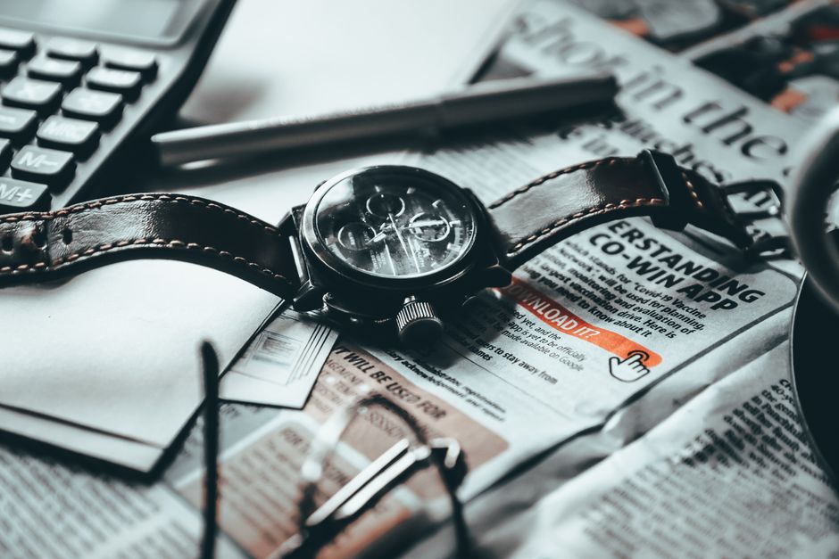 High angle of wristwatch placed on newspaper next to papers with calculator near pen and eyeglasses on table in light room