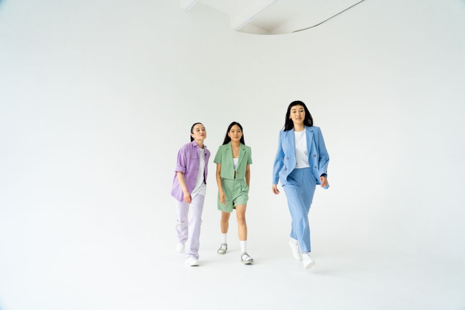 Three young women in trendy pastel suits walking confidently in studio with white background.
