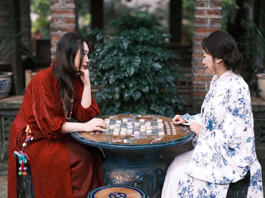 Two women in traditional attire engage in a board game outdoors, reflecting cultural heritage and leisure.