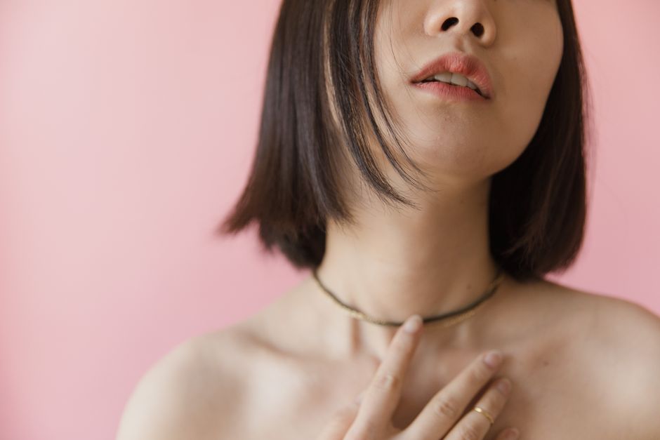 Elegant close-up of a woman with a necklace and soft pink background.