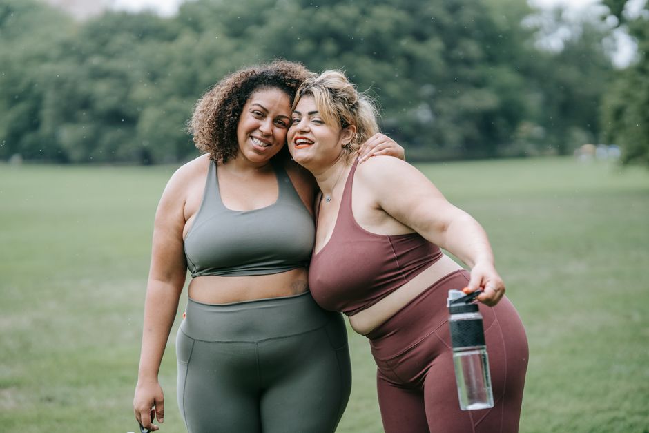 Two women smiling and hugging each other in sports clothing on a grassy field.