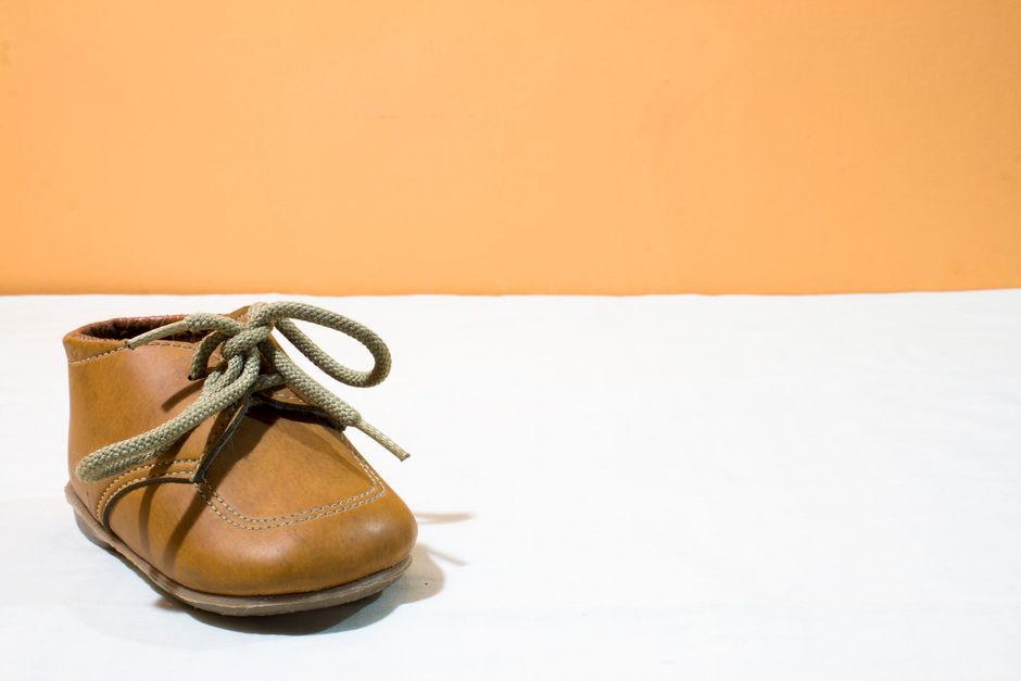 Close-up of a brown leather baby shoe with tied shoelaces on a white and orange background.