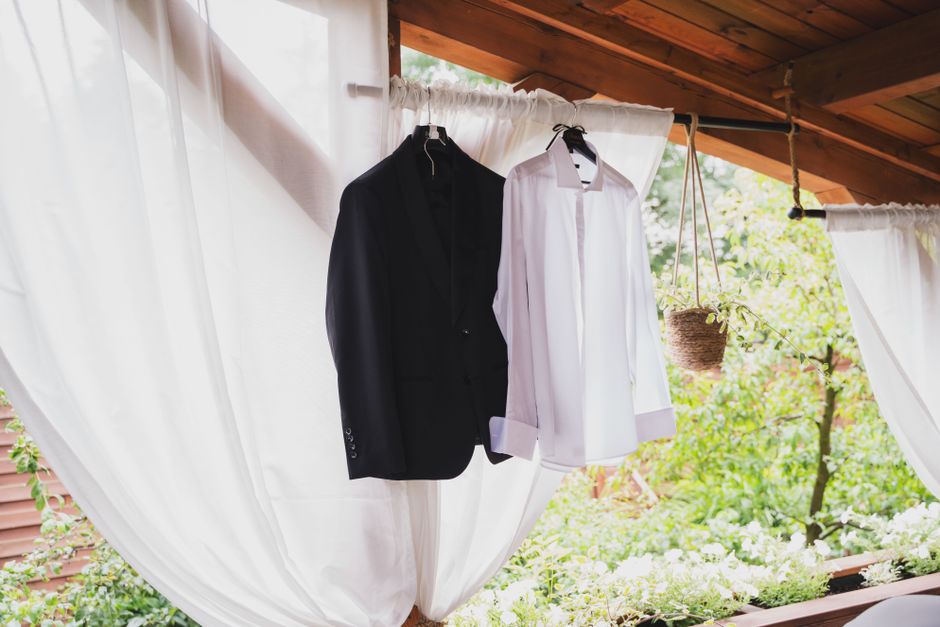 A black suit and white shirt hanging outdoors on a wooden frame, surrounded by nature.