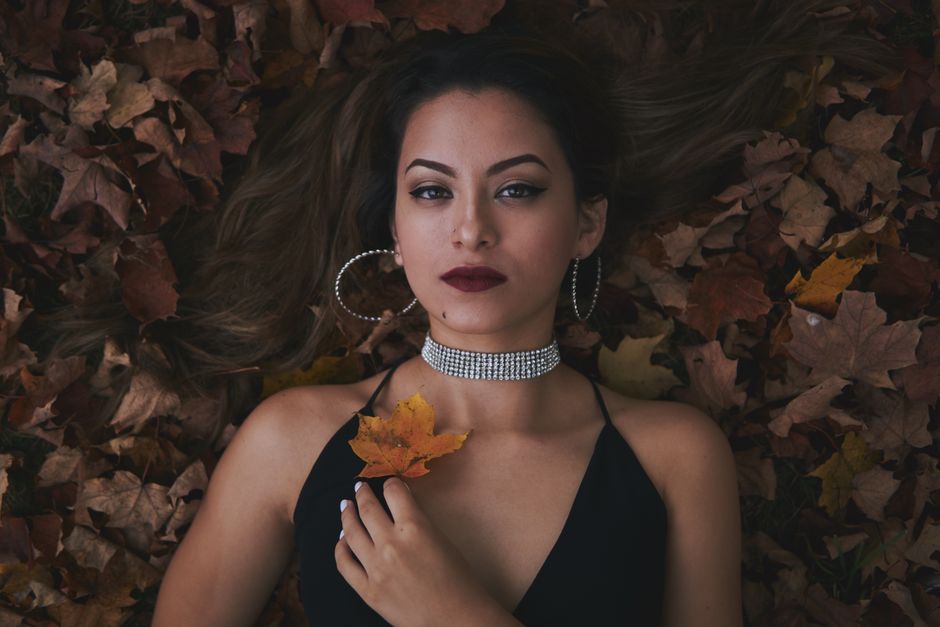 A woman in elegant fashion lies on autumn leaves, showcasing jewelry and style.