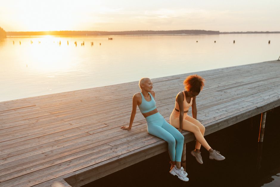 Two women enjoying a peaceful sunset on a lakeside jetty, embracing outdoor tranquility.