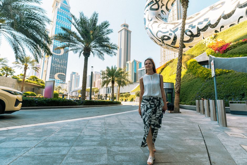 A woman walking in Dubai among palm trees and futuristic architecture, showcasing urban elegance.