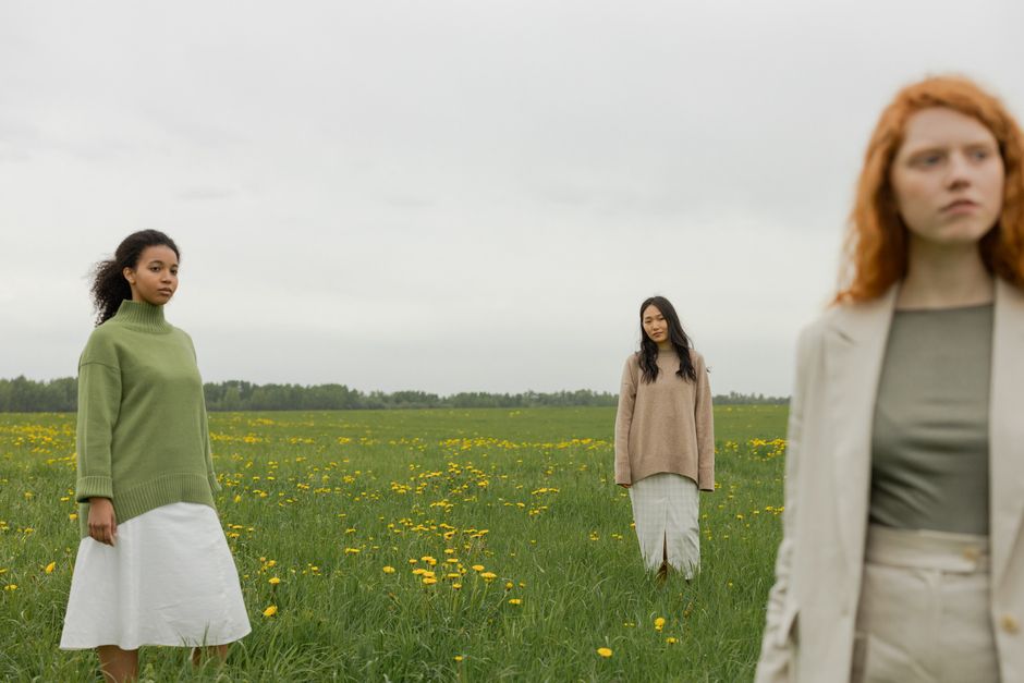 Three diverse women standing in a green field with yellow flowers, showcasing friendship and diversity.