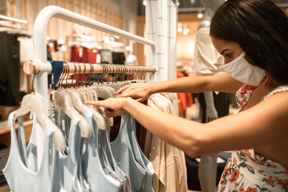 Woman wearing a face mask shopping for clothes in a store, reflecting the pandemic's new normal.