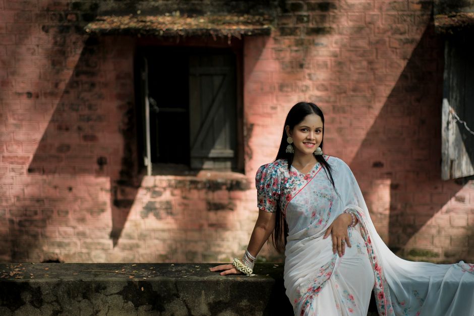 Smiling woman in a floral sari posing against a brick wall in Chattogram, Bangladesh.