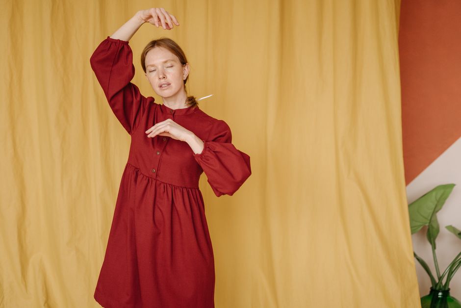 Woman in red dress posing gracefully against yellow background in a serene indoor setting.