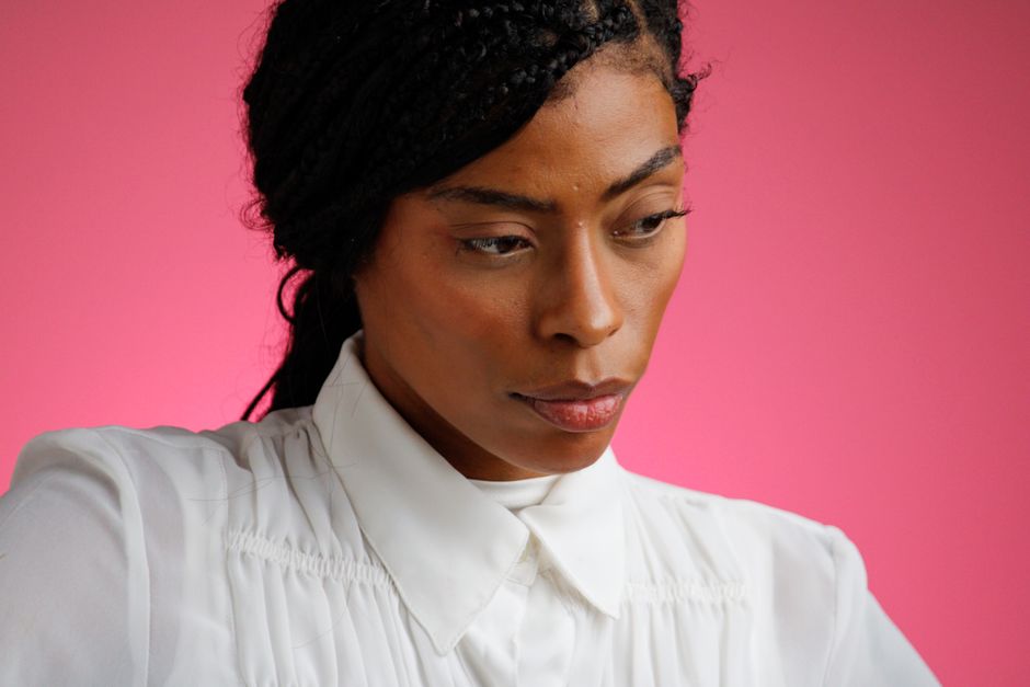 Close-up portrait of a woman deep in thought against a bright pink backdrop.