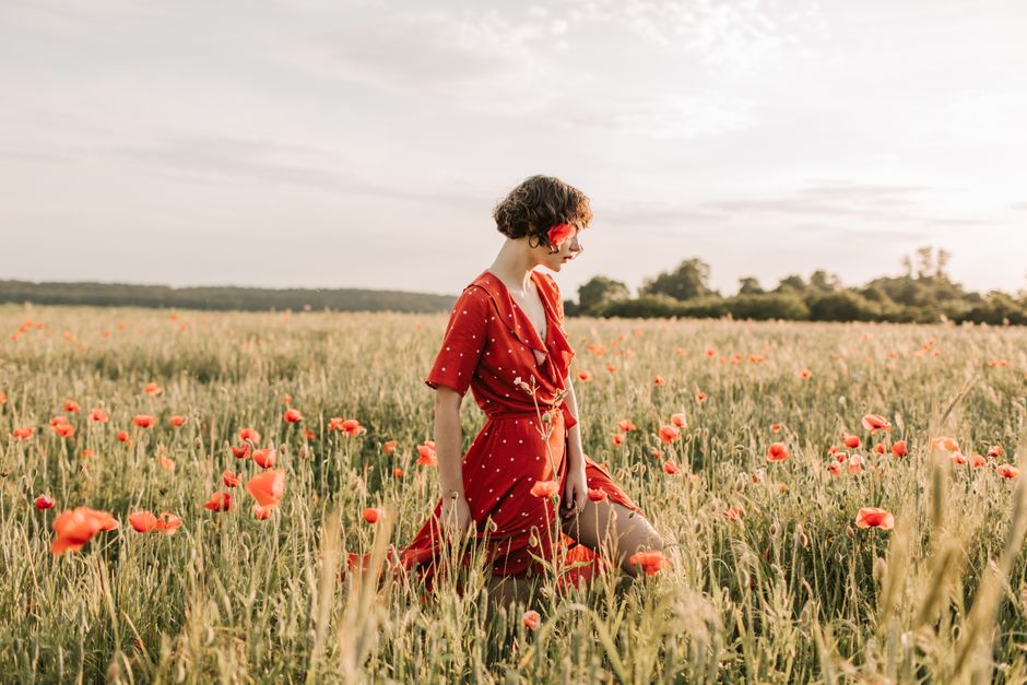 A serene image of a woman in a red dress walking through a field of poppies on a sunny day.