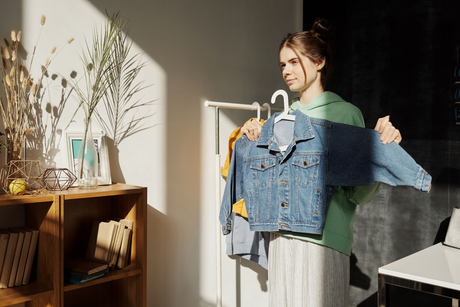 A teenage girl holding a denim jacket in a sunny indoor room.