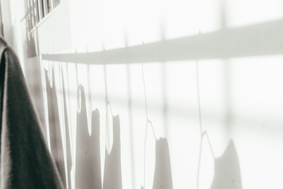 Abstract photo showcasing shadows of clothes and hangers cast on a sunlit wall.