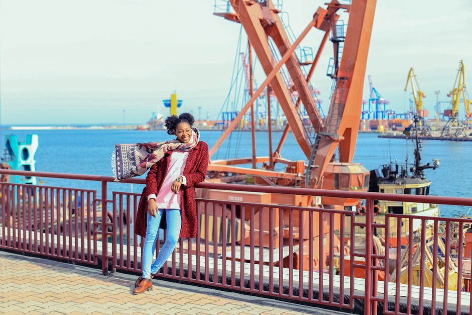 Smiling young adult poses at Odesa seaport with colorful cranes and ocean view.