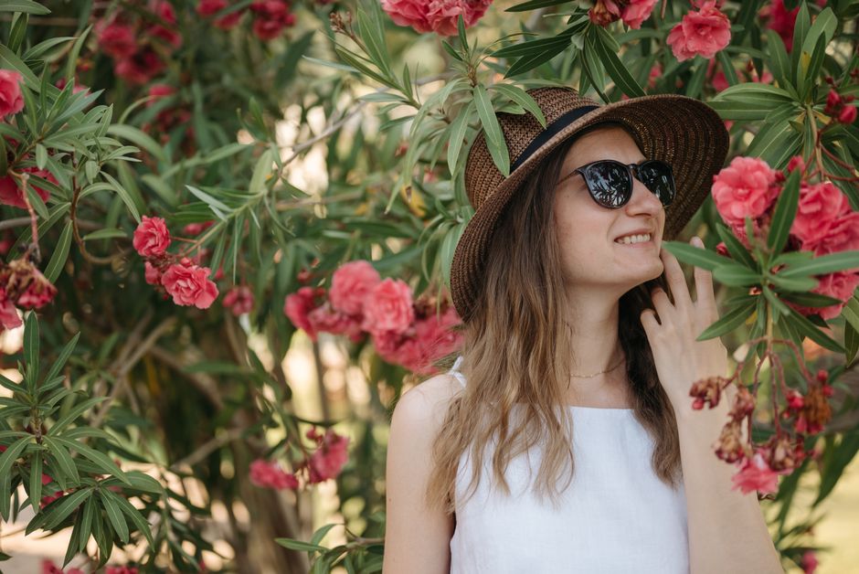 Smiling woman in hat among vibrant pink flowers outdoors.
