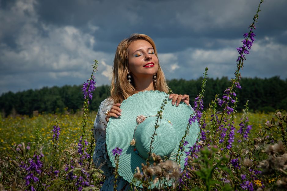 A woman holds a turquoise hat in a wildflower field on a summer day, enjoying nature.
