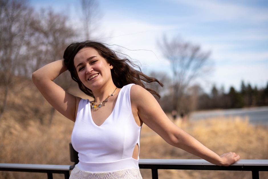Smiling woman in a white dress outdoors enjoying a sunny and windy spring day.