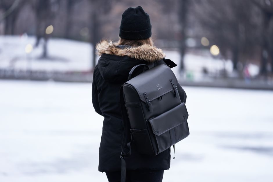 A woman in a black winter jacket explores a snowy park with a stylish backpack.