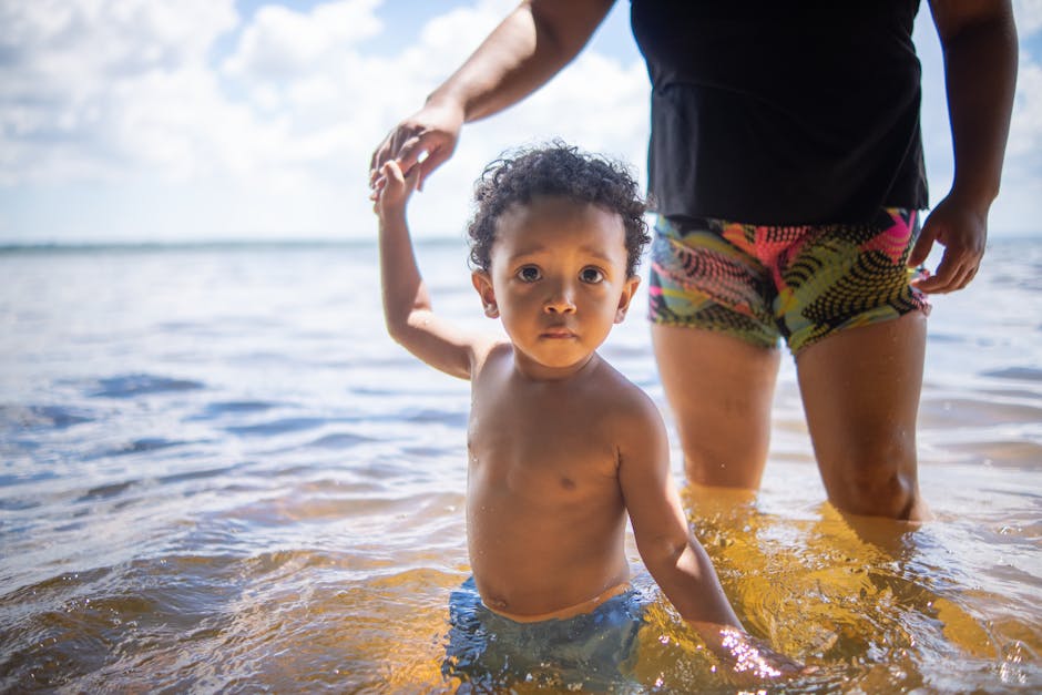 A happy child playing in the water at a sunny beach with a guardian.