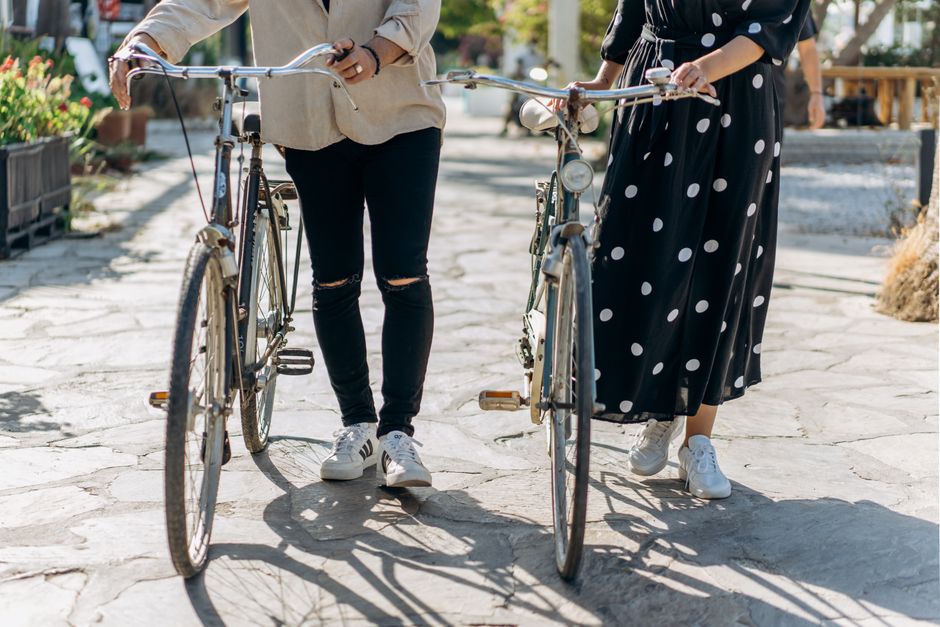 Two adults walking their bicycles on a sunlit street.