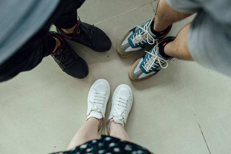 Overhead view of three people wearing different sneakers standing together indoors in Đà Lạt, Vietnam.