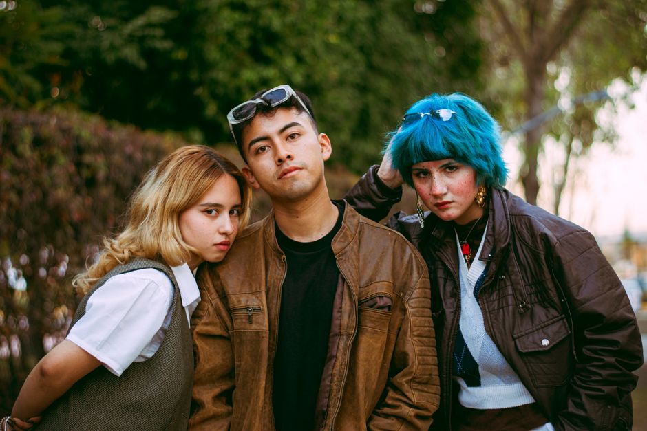 Three young adults showcase edgy and unique street fashion in an outdoor setting.