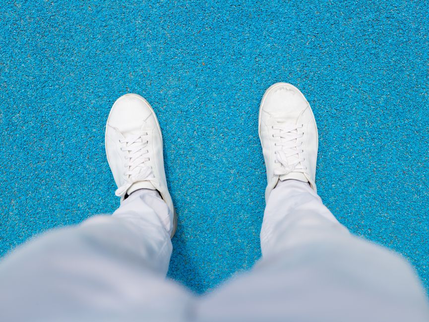 White sneakers paired with sweatpants on a vibrant blue surface, viewed from above.