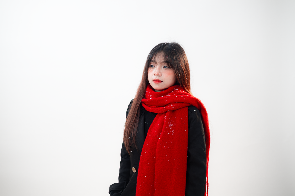 Portrait of a woman wearing a red scarf, gazing thoughtfully with snowflakes on her.